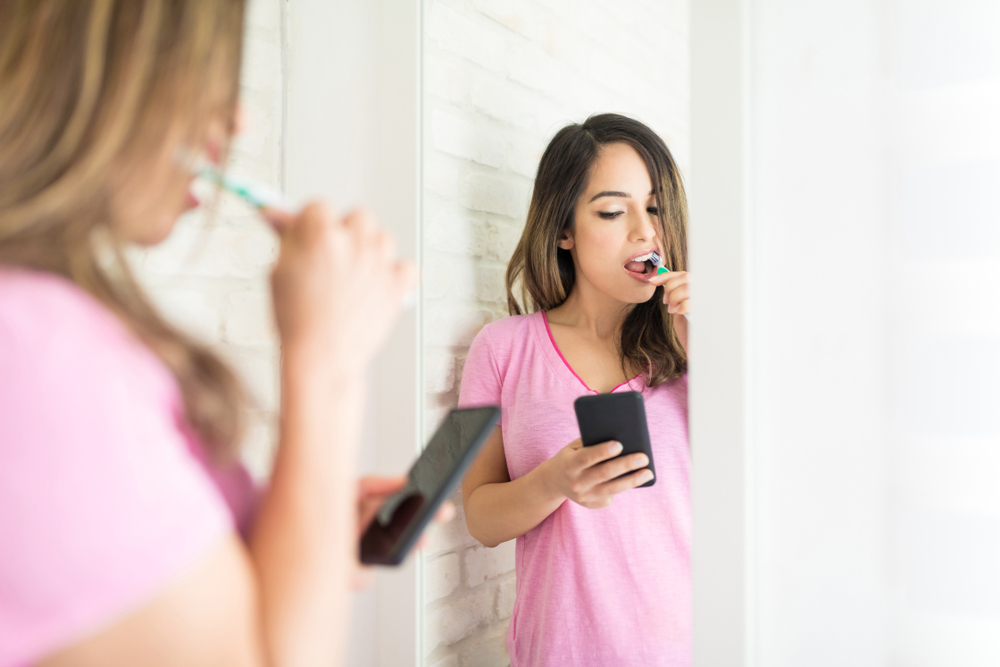 Woman brushing teeth while looking at her phone